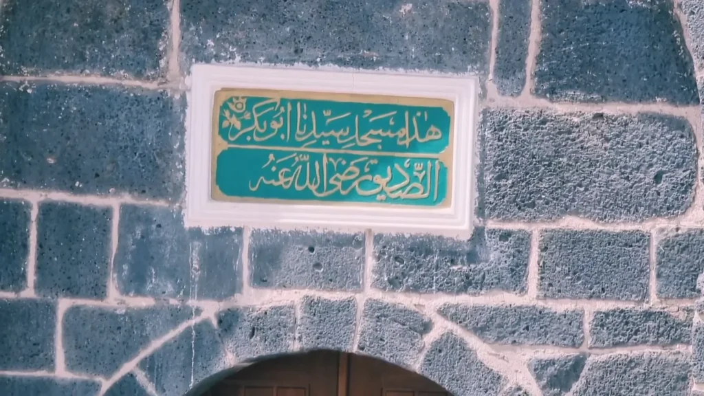 Arabic calligraphy nameplate of Masjid Abu Bakr Siddiq RA mounted on black basalt wall in Madinah’s historic Musalla zone near Masjid al-Ghamamah